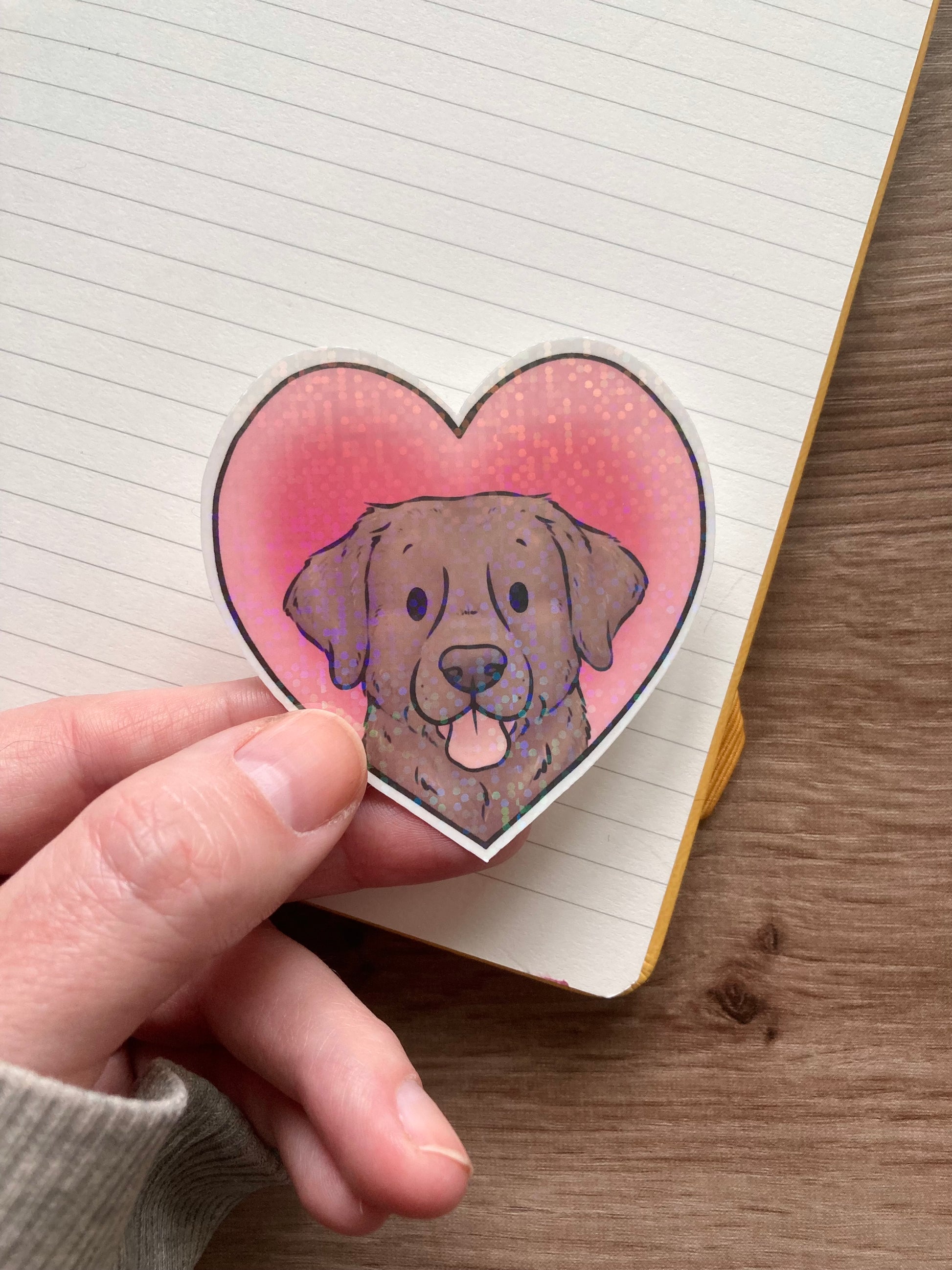 Heart-shaped sticker with a dog design held over a lined notebook
